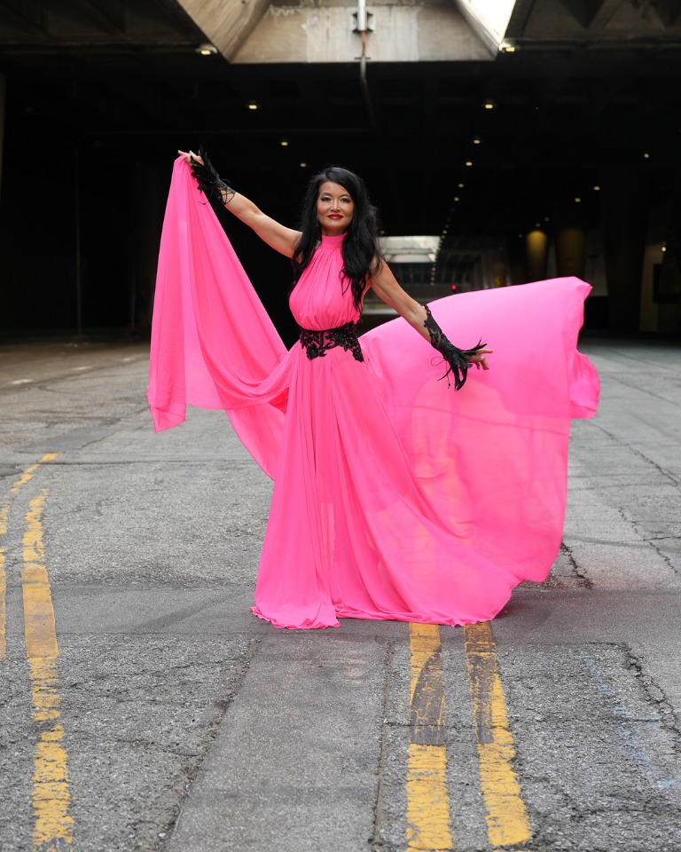 Model in a flowing bright pink dress in an urban setting
